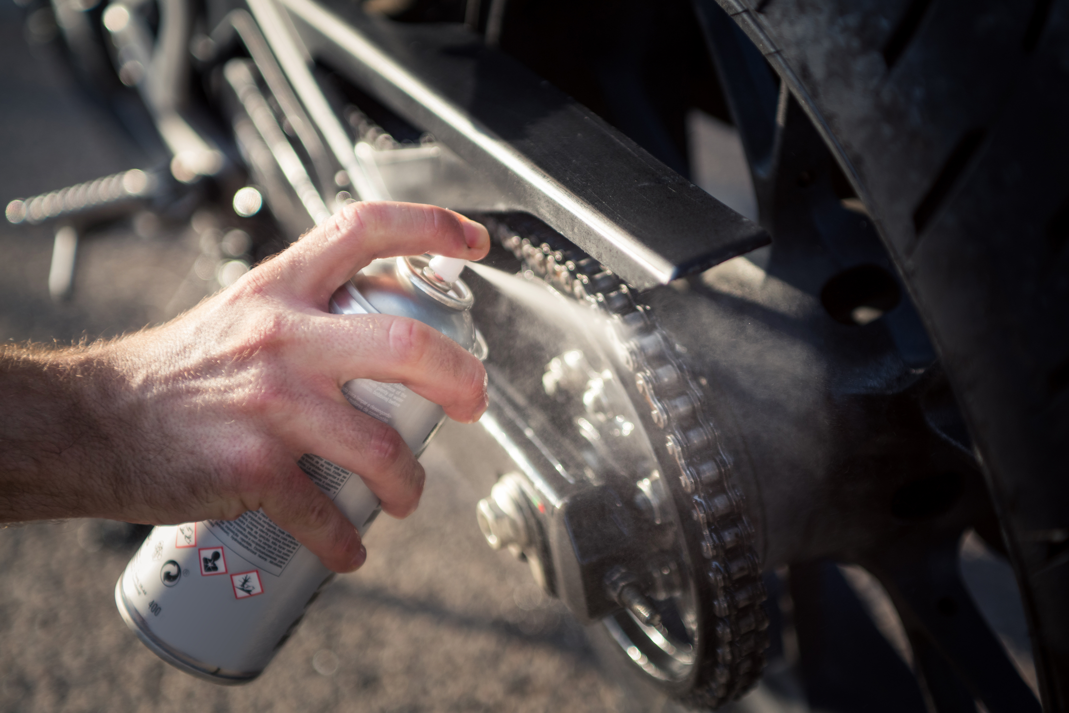 hand using spray can to clean and protect motorbike chain